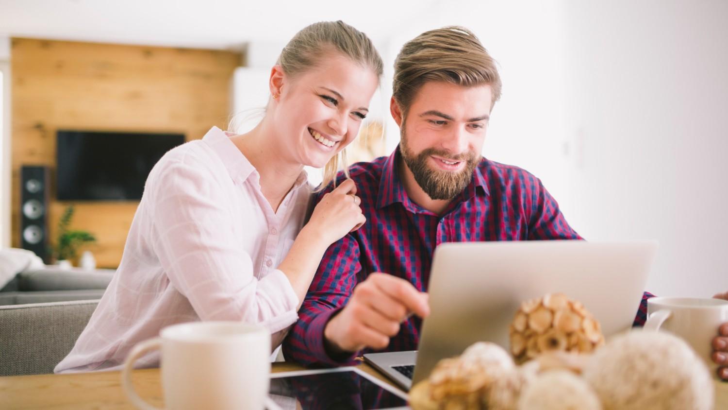 A young man and woman smile as they sit next to each other at a table and read about the Revolut Business Account on their laptop